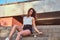 Young beautiful girl dressed in shorts and t-shirt sitting on a skateboard at steps on bridge background.