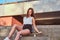 Young beautiful girl dressed in shorts and t-shirt sitting on a skateboard at steps on bridge background.