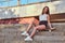 Young beautiful girl dressed in shorts and t-shirt sitting on a skateboard at steps on bridge background.