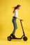 Young beautiful girl with electric scooter. Isolated on yellow background. Technology and freedom of movement.