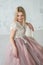 Young beautiful girl in an evening dress with lace and pink fartine on the background of a white textural wall.