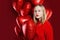 Young beautiful girl holds balloons red heart on red background