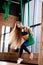 Young beautiful girl with long blond hair dressed in the sport clothes is doing fitness on the green aerial silk in the