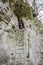 Young beautiful girl with long hair in a down jacket, climbed to the highest ladder in the cave in the rock