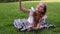 Young beautiful girl making selfie portrait using smartphone in green park, lying on the grass with mobile phone