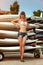 Young beautiful girl at old surfing and windsurfing station stands near the surfboards installed on the racks outdoor