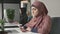 Young beautiful girl in pink hijab sits in office and uses smartphone. Girl in black hijab in the background. Arab women