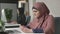 Young beautiful girl in pink hijab sits in office and uses smartphone. Girl in black hijab in the background. Arab women