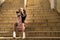 Young and beautiful girl with punk style sitting on some stairs leaning on a skateboard that she has between her legs