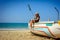 Young beautiful girl in short transparent dress and straw hat sits on a wooden fishing boat against blue sea on hot tropical day