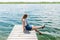 Young beautiful girl sitting on jetty river on background