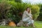 Young beautiful girl sitting on the stone near the tropical palm tree