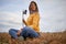 A young beautiful girl with the skateboard is sitting and relaxing on a meadow. Nature, relaxation, outside