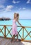 Young beautiful girl stands in pink sundress on sundeck of villa on water, Maldives