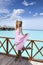 Young beautiful girl stands in pink sundress on sundeck of villa on water, Maldives