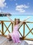 Young beautiful girl stands in pink sundress on sundeck of villa on water, Maldives