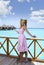 Young beautiful girl stands in pink sundress on sundeck of villa on water, Maldives