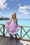 Young beautiful girl stands in pink sundress on sundeck of villa on water, Maldives