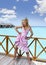 Young beautiful girl stands in pink sundress on sundeck of villa on water, Maldives