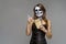 Young beautiful girl with a sugar skull make up, holds in her hand a paper box for instant noodles and chopsticks. Halloween face