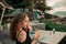 Young beautiful girl in summer bar with cocktail at sunset near the beach