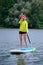 Young beautiful girl-surfer riding on the stand-up paddle board in the clear waters of the on the background of green trees