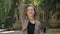 Young beautiful girl is touching hair in park in daytime in summer, smiling, watching at camera