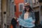 Young beautiful girl tourist stands on a road of cobblestones, looks at a map and considers where to go