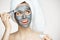 Young beautiful girl in towel on head covering face with mask smiling over white background. Beauty cosmetology and spa.