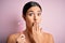 Young beautiful girl using shaver for depilation standing over isolated pink background cover mouth with hand shocked with shame