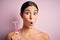 Young beautiful girl using shaver for depilation standing over isolated pink background scared in shock with a surprise face,