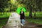 Young beautiful girl walking alone under green umbrella in the city park in summertime