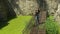 Young beautiful girl walks on thin ruined rusty metal bridge over green water.