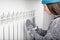 Young beautiful girl warms hands near a radiator