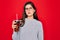 Young beautiful girl wearing glasses drinking sweet drink soda over red background with a confident expression on smart face