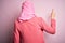 Young beautiful girl wearing muslim hijab standing over isolated pink background Posing backwards pointing ahead with finger hand