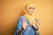 Young beautiful girl wearing muslim hijab standing over isolated yellow background afraid and terrified with fear expression stop