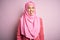 Young beautiful girl wearing muslim hijab standing over  pink background sticking tongue out happy with funny expression
