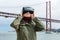 Young beautiful girl wearing virtual reality glasses. 25th of April bridge in Lisbon in the background. The concept of