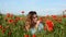 Young beautiful girl weaves a bouquet of poppies with a poppy field on a sunny summer day
