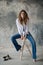 Young beautiful girl in a white shirt and flared jeans in a loft studio on a bar stool on a gray concrete background