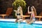 Young beautiful girls smiling, greeting, relaxing near swimming pool.