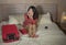 Young beautiful and happy Asian Chinese woman in chic dress sitting happy in room bed with luggage after hotel check in excited