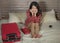 Young beautiful and happy Asian Korean woman in chic dress sitting happy in room bed with luggage after hotel check in excited