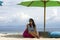 Young beautiful and happy Asian Korean woman in chic Summer dress and sunglasses posing relaxed at tropical beach relaxed sitting