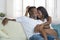 Young beautiful and happy black African American couple in love relaxed at modern home living room cuddling sweet on sofa couch