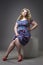 Young beautiful happy blonde plus size model in dress and shoes, xxl woman on gray studio background