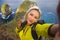 Young beautiful and happy hiker woman with backpack hiking on sea mountain cliff taking selfie portrait with mobile phone enjoying