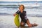 Young beautiful and happy surfer woman sitting on beach sand holding yellow surf board smiling cheerful enjoying summer holid