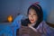Young beautiful and happy sweet Asian Korean teen girl with in headband and pajamas enjoying with mobile phone in bed at night